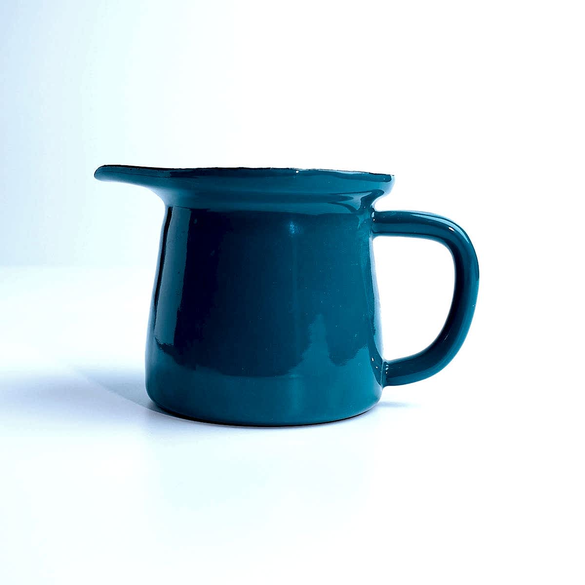 Beyaz zemin üzerinde duran, kulplu ve ağızlı, parlak petrol yeşili emaye sosluk.